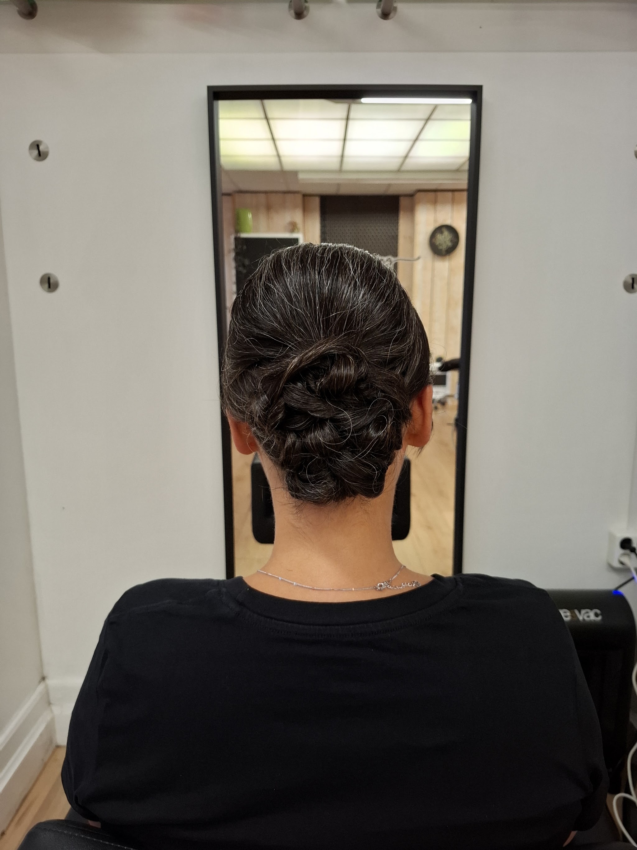 Een opgestoken kapsel van achteren gezien, met lange zwarte oorbellen, in de spiegel van de salon