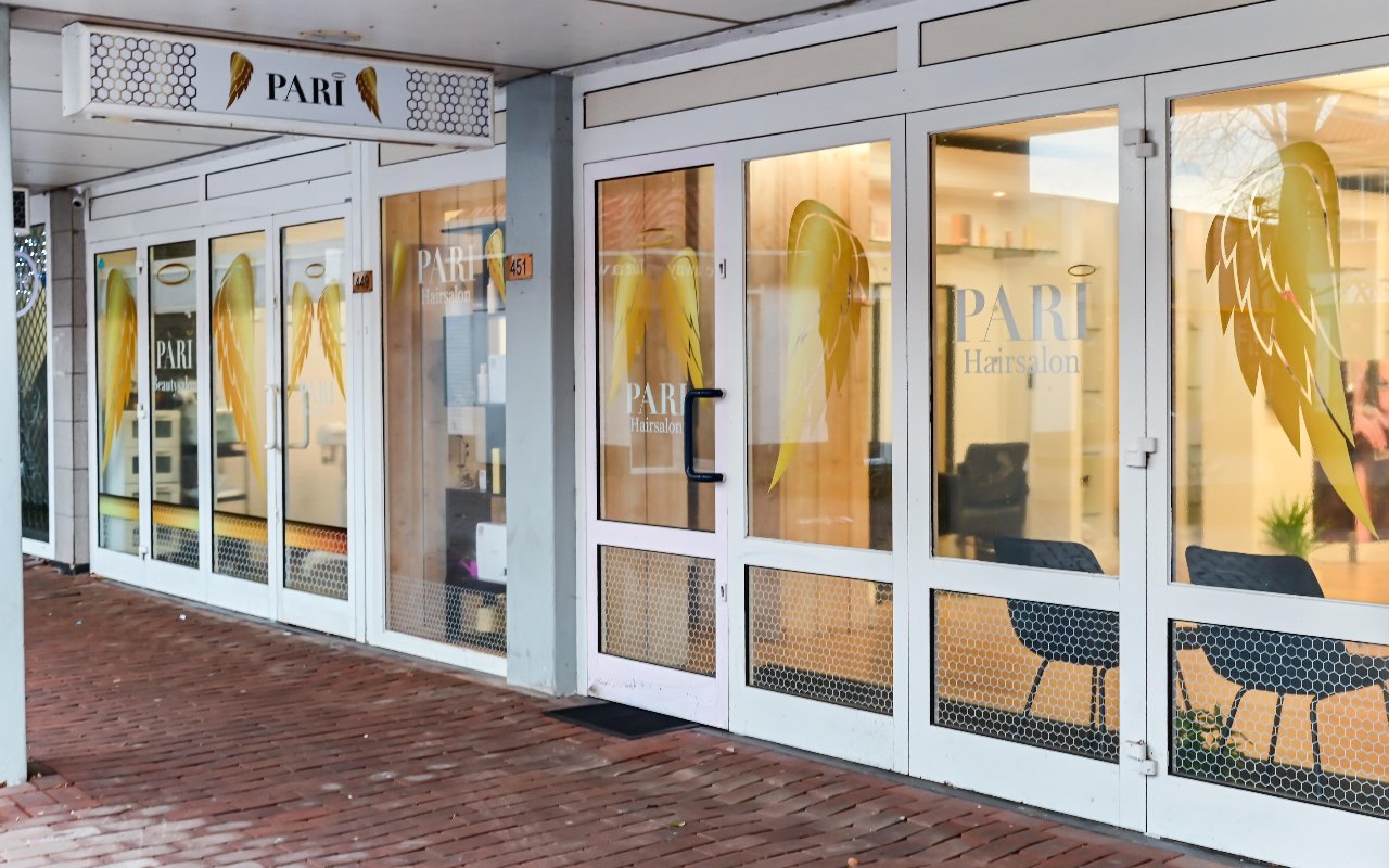 De glazen pui van Pari onder de overkapping, met het PARI-bord en gouden vleugels op de deuren